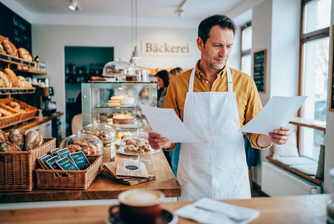 Bäckereibesitzer steht in seiner Bäckerei und liest Dokumente