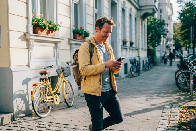 Mann geht am Gehsteig mit Smartphone in der Hand